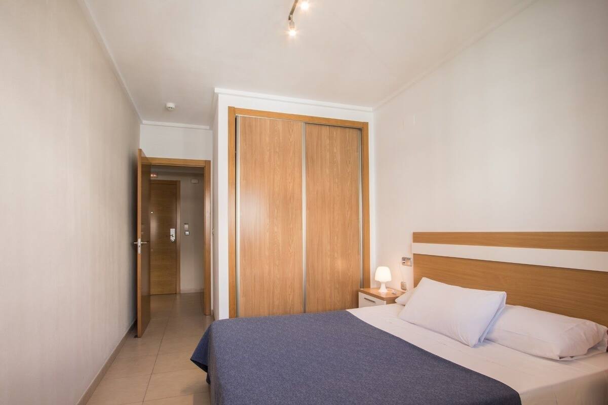 A hotel room with a bed, a nightstand, a wooden wardrobe, and a door leading to another room.