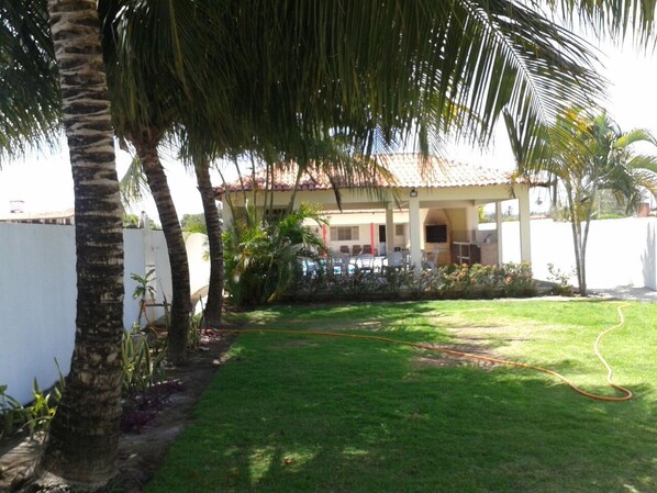 A well-maintained garden with a lawn, palm trees, and a building with a tiled roof.