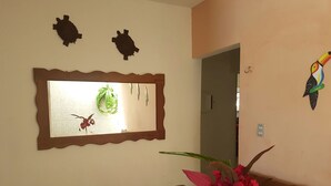 Et værelse med et træbord, et spejl med dekorativ ramme, en vase med blomster og vægdekorationer, herunder en fugl og en skildpadde.