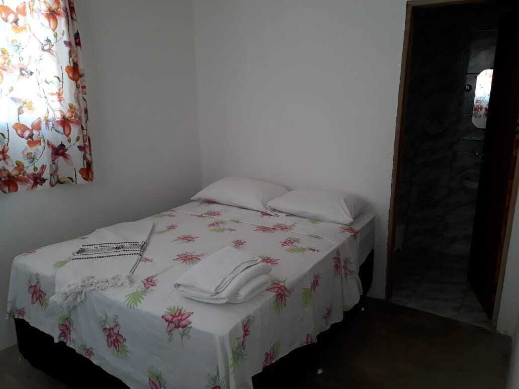 A small, neatly made bed with floral bedding and white pillows in a room with plain walls and a stone wall entrance.