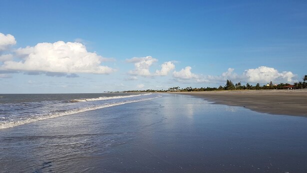 En strand med bred sandstrand, rolige bølger og klar himmel.