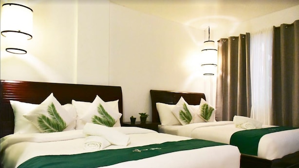 A hotel room with two beds, each with white bedding and green accents, and a wooden headboard. - Cocotel room at Chartel Inn Boracay (Malay)