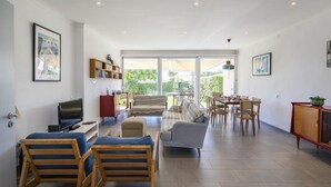 Un salón amplio con televisor, sofá, sillones, una mesa de comedor y una estantería.