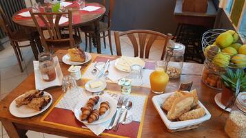 Una tavola imbandita per la colazione con croissant, pane, burro, marmellata e succo d'arancia.