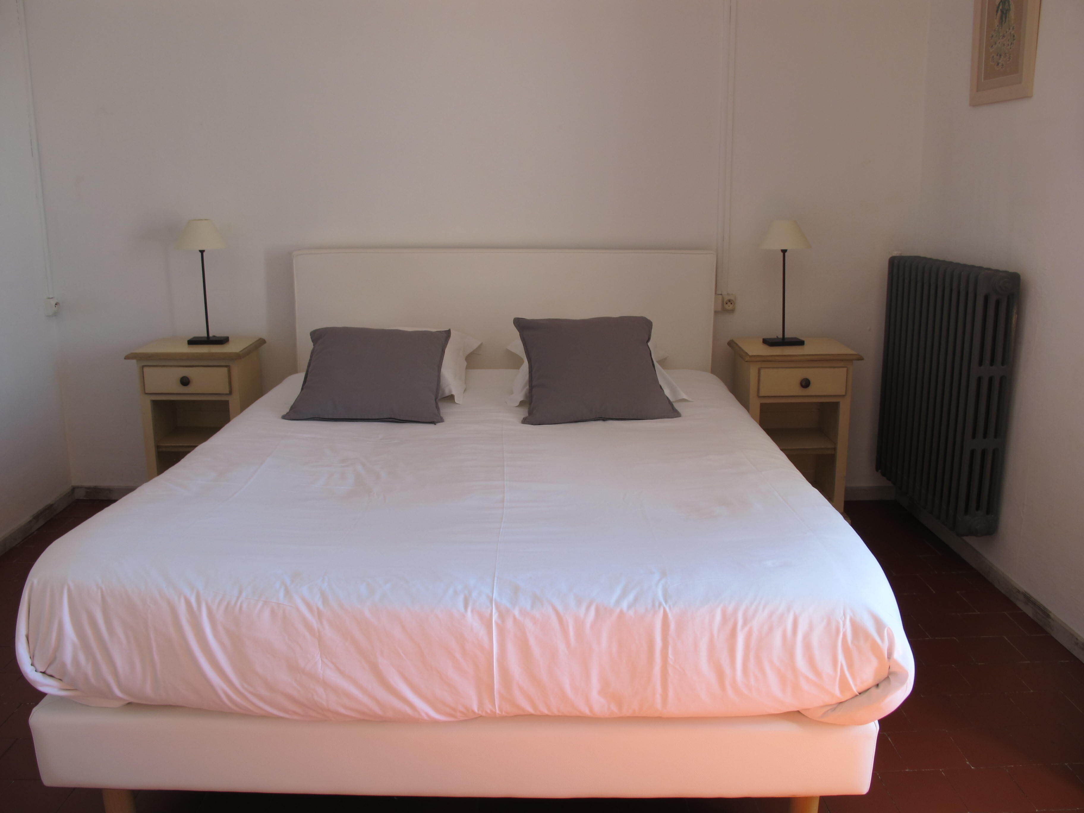 Un lit bien fait, avec deux oreillers, une table de chevet avec une lampe et un radiateur au mur.