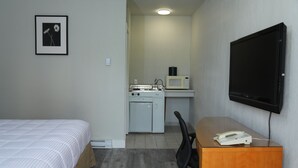 A hotel room with a bed, a desk with a telephone, a microwave, and a television on the wall.