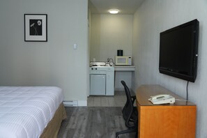 A hotel room with a bed, a desk with a telephone, a microwave, and a television on the wall. - Fraser Inn (Prince George)