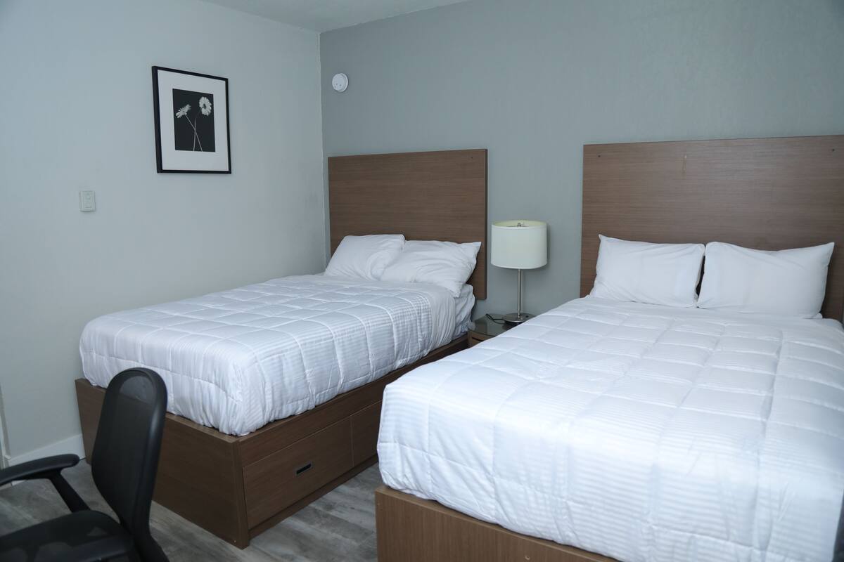 Ett hotellrum med två separata sängar, ett skrivbord, en stol, en sänglampa och en inramad tavla på väggen.