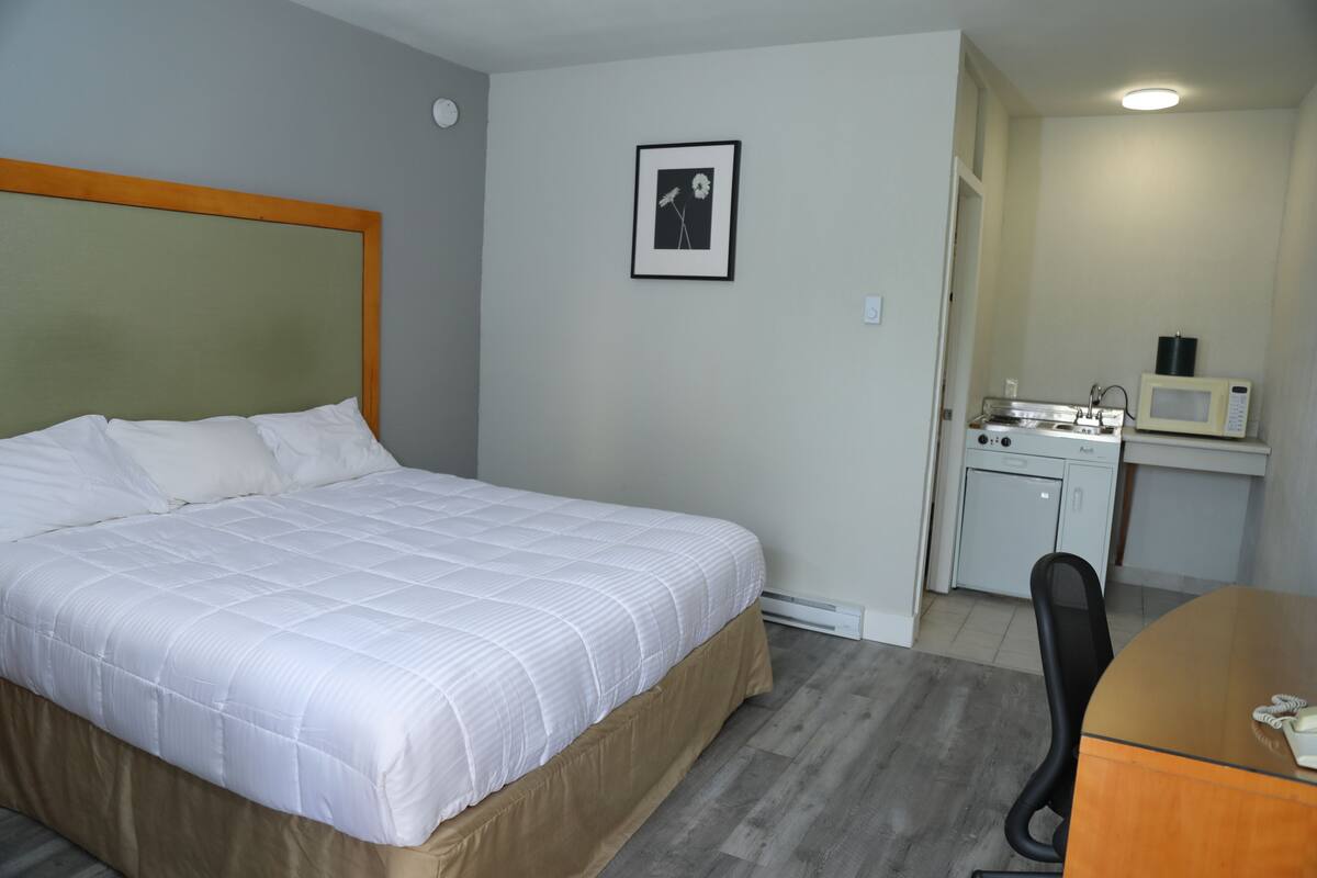 Ett hotellrum med en säng, ett skrivbord, en stol, en mikrovågsugn och ett litet pentry.