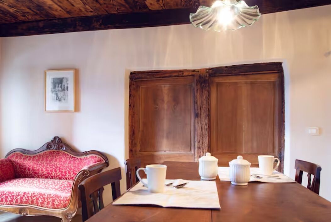 A dining area with a wooden table set for two, a red upholstered chair, and a wooden door in the background.