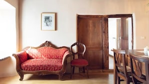 Une pièce avec un plafond en bois, un canapé rouge à motifs, une chaise en bois, une table à manger avec des chaises et une porte en bois.