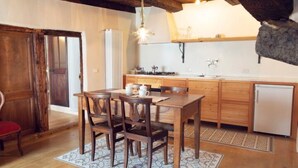 Une cuisine rustique avec des meubles de rangement en bois, une table à manger avec des chaises, un luminaire suspendu et un petit réfrigérateur.