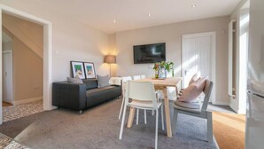 Ein modernes Wohnzimmer mit einer Couch, einem Esstisch, Stühlen und einem Fernseher.