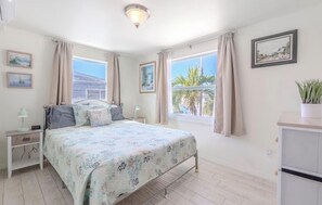 Ein Schlafzimmer mit Bett, Nachttischen, einem Schminktisch und einem Fenster mit Vorhängen.