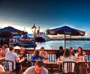 Un restaurant situé au bord de l’eau, avec une terrasse, des tables et des parasols.