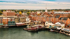 Ein Stadtbild am Wasser mit historischen Gebäuden, einem markanten Turm und vor Anker liegenden Booten.
