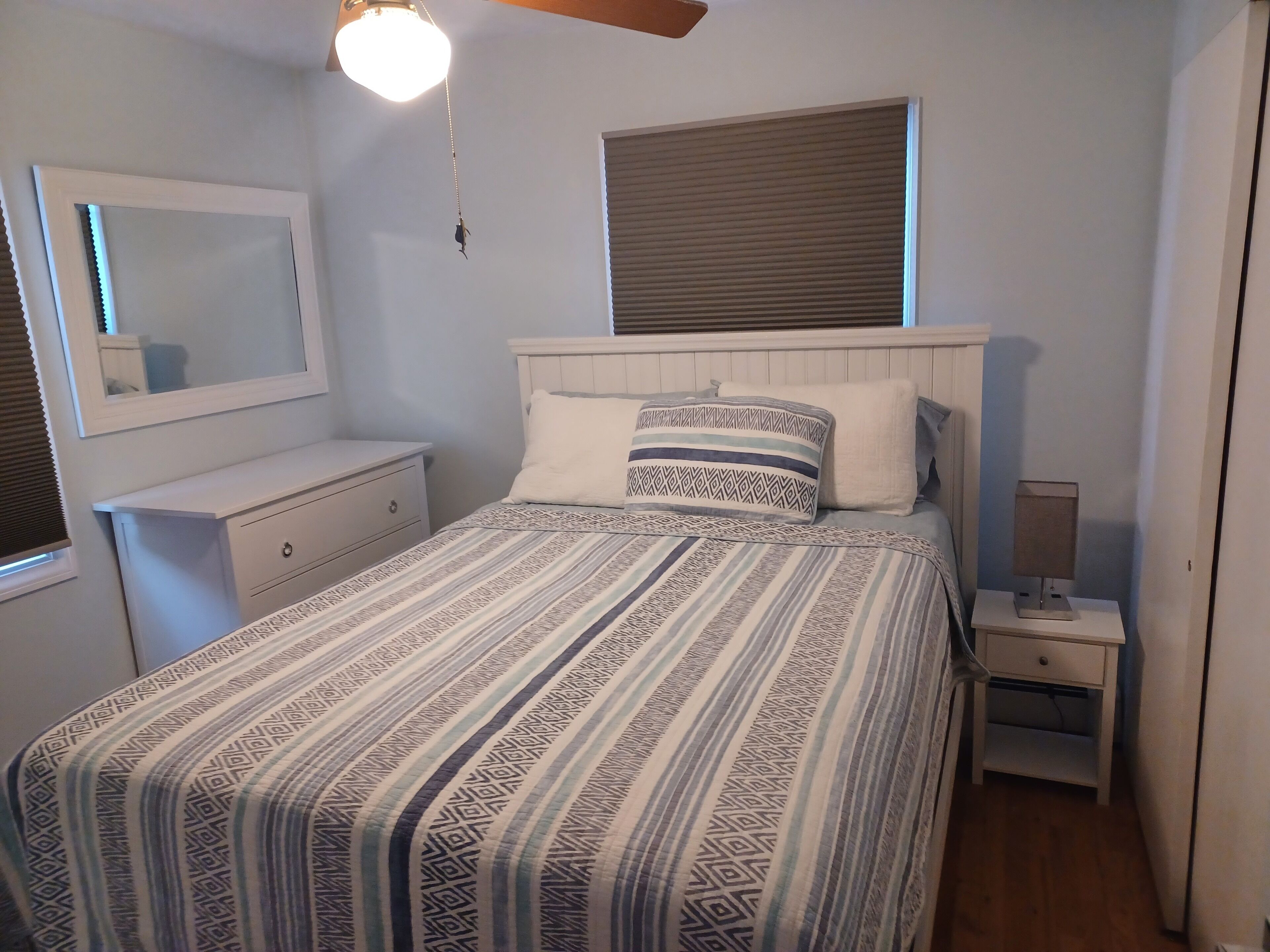 Une chambre à coucher comprenant un lit, une table de chevet, une commode, un miroir et un luminaire suspendu.
