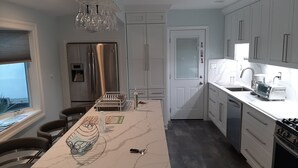 Ett modernt kök med vita skåp, ett kylskåp i rostfritt stål, en inbyggd ugn och en bänkskiva i marmor.