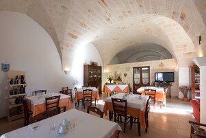 A dining area with multiple tables and chairs, a television, and a kitchen area with a brick wall and arch.