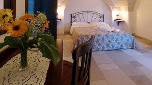 Ein Schlafzimmer mit einem Bett, einem Sessel, einem Tisch mit Blumenvase und einer Deckenleuchte.