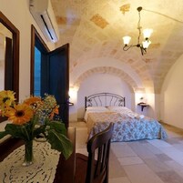 Een slaapkamer met een bed, een stoel, een tafel met een bloevas en een plafond met een lamp.