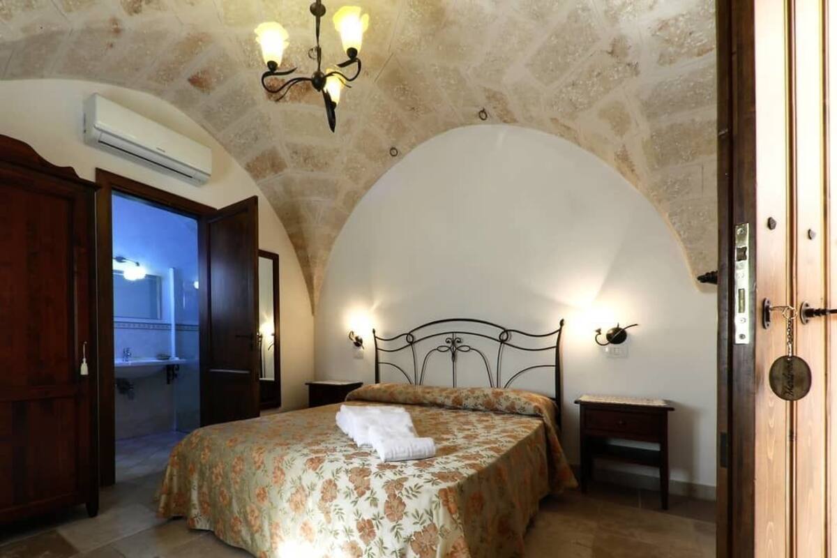 Une chambre à coucher avec un lit, un lustre, une porte en bois et un mur en pierre.