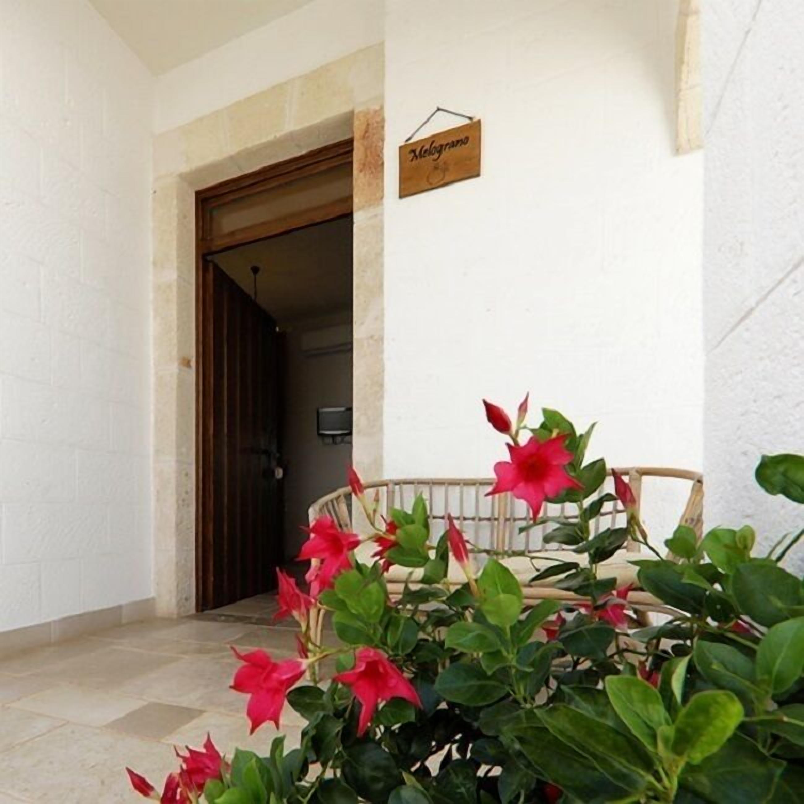 Entrada de hotel con un letrero de madera, una silla y flores rojas.
