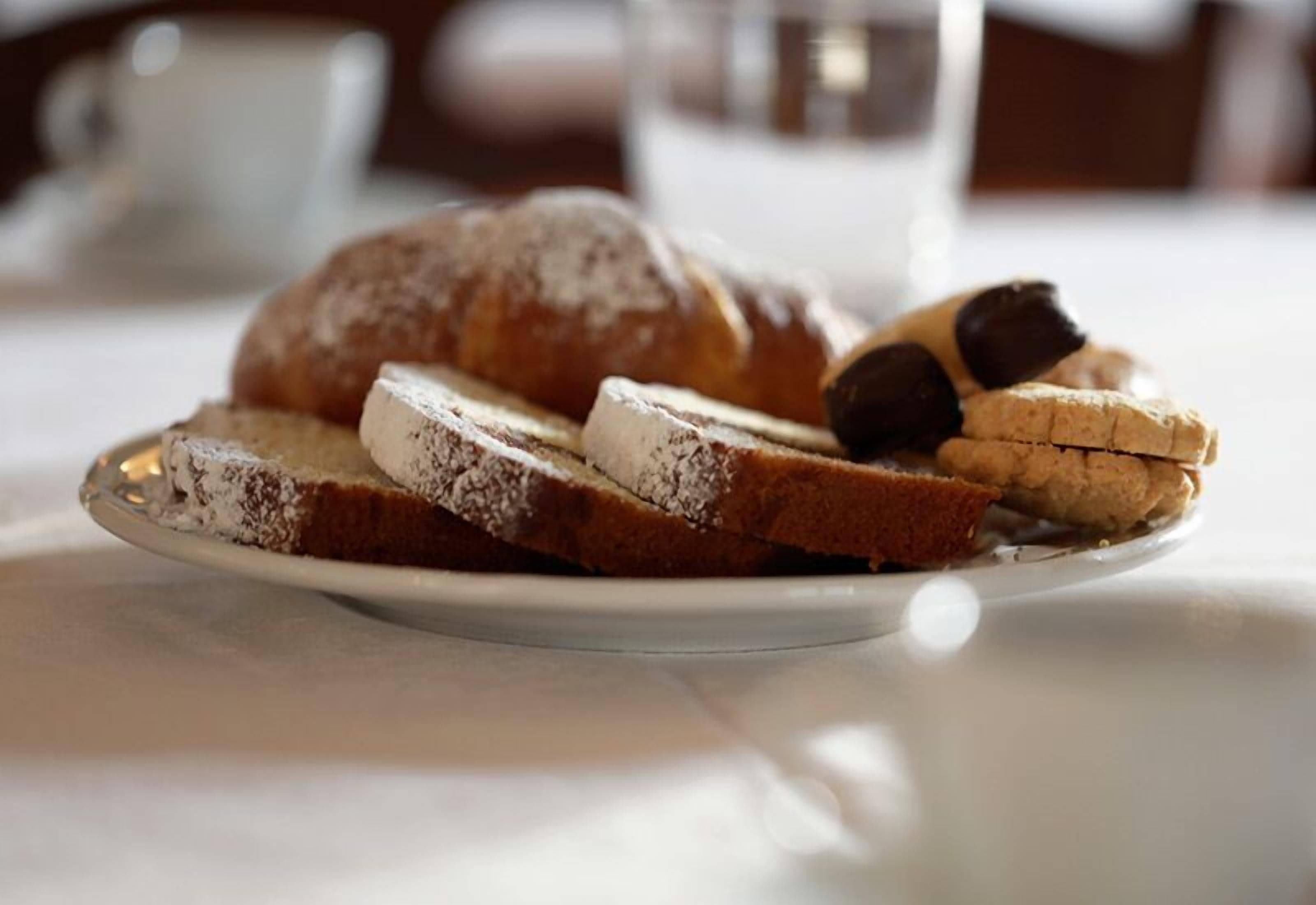 Um prato com fatias de bolo e um croissant sobre uma mesa.