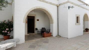 Un bâtiment blanc doté d’un patio carrelé, de deux arcades et d’un petit espace de détente avec des chaises et une table.