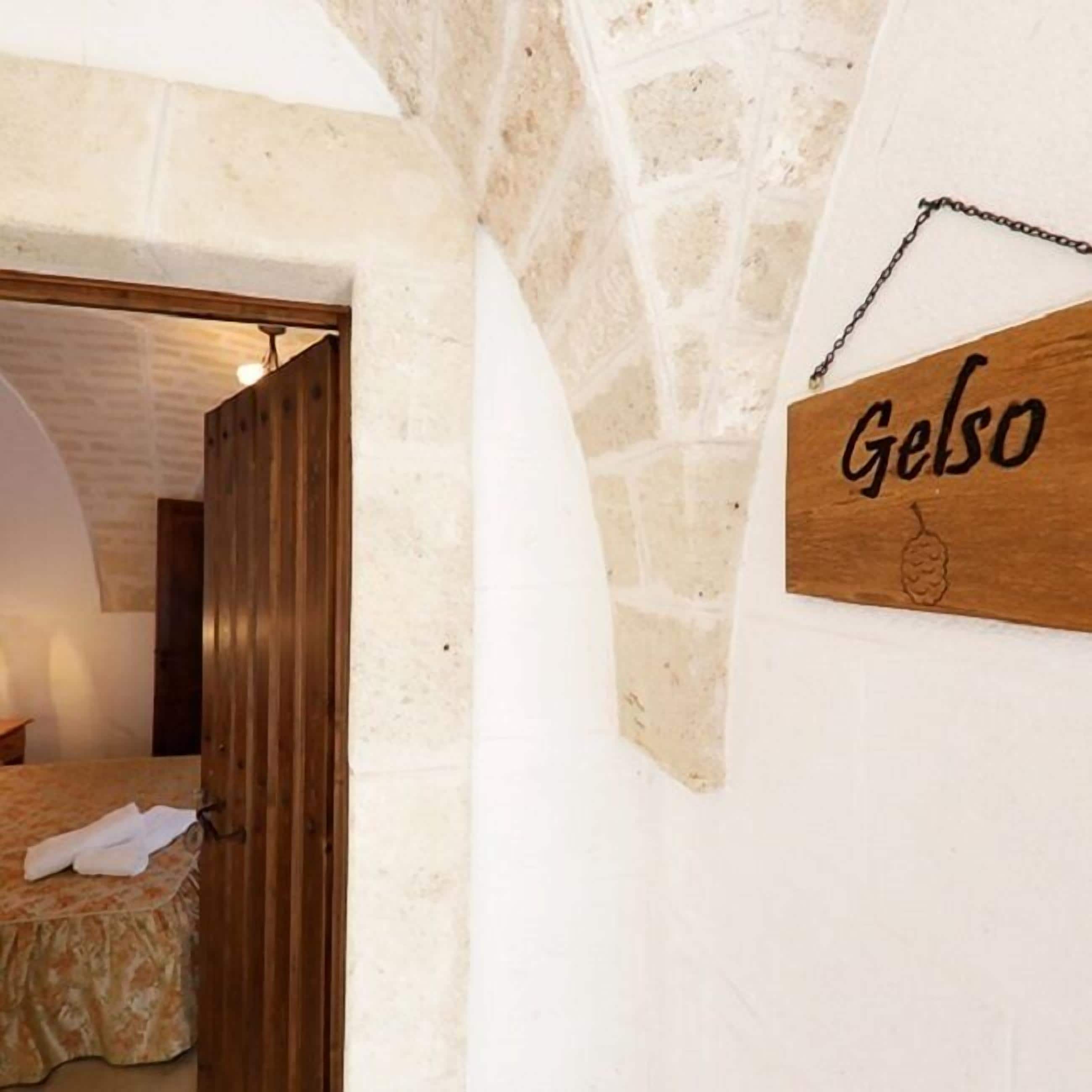 A room with a stone wall, a wooden door, and a sign that reads "Gelso".
