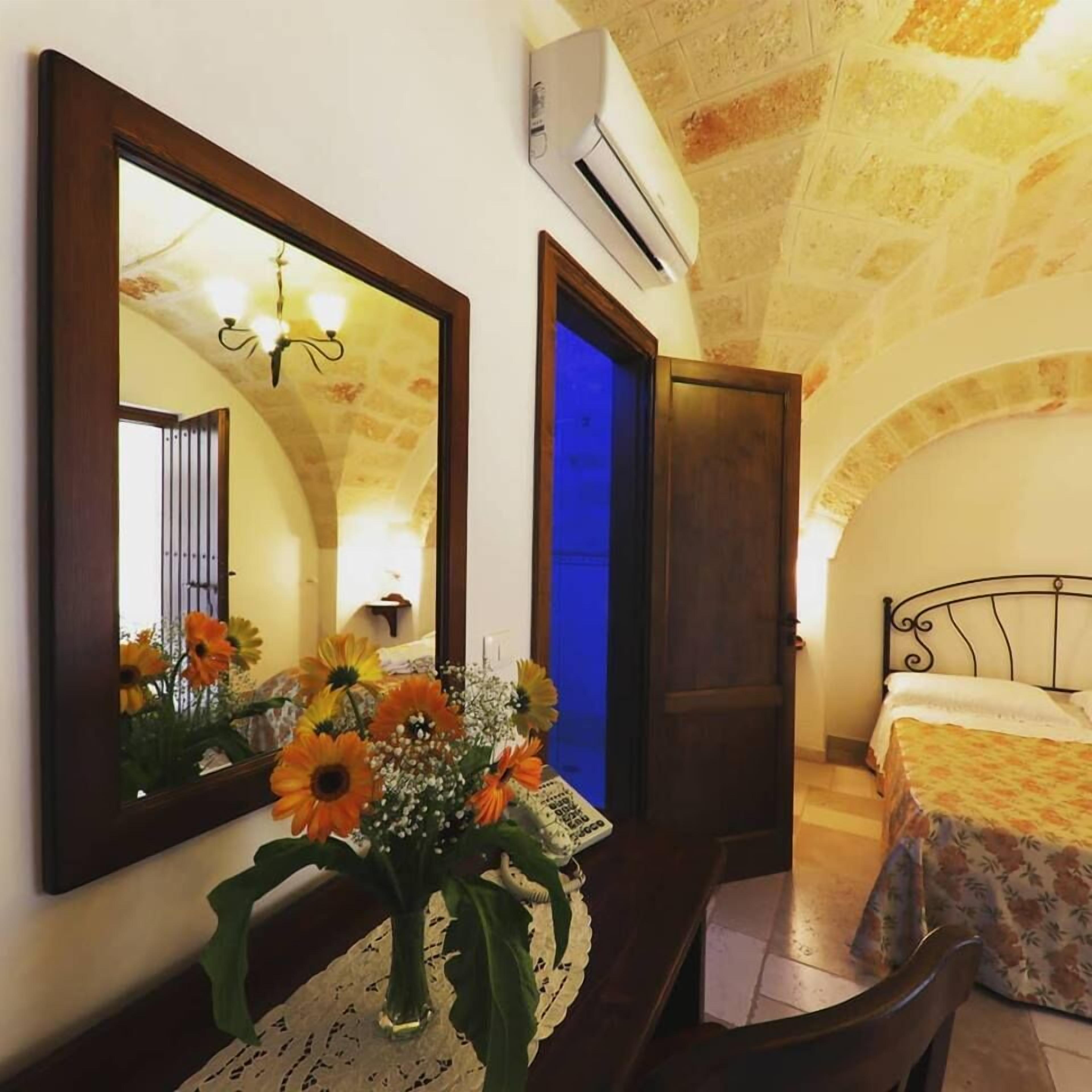A room with a bed, a dresser, a mirror, and a vase of flowers.