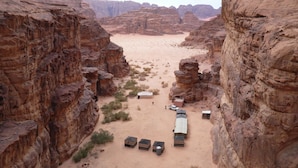 Un canyon désertique avec des formations rocheuses, des tentes et quelques véhicules.
