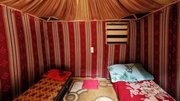 Une chambre avec deux lits simples, des murs rayés rouge et beige, une petite fenêtre et un luminaire suspendu.