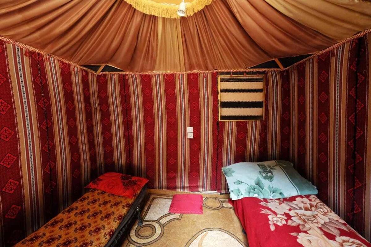 A room with two single beds, striped red and beige walls, a small window, and a hanging light fixture.