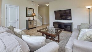 A living room with a sofa set, a coffee table, a TV, and a staircase in the background. - 5BR Disney Pool Home | 3 King Bedrooms | Private Pool, Spa & BBQ | Sleeps 13 (Kissimmee)