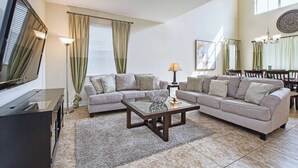 A living room with a TV, two sofas, a coffee table, and a dining area with chairs. - 5BR Disney Pool Home | 3 King Bedrooms | Private Pool, Spa & BBQ | Sleeps 13 (Kissimmee)