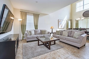 A living room with a TV, two sofas, a coffee table, and a dining area with chairs. - 5BR Disney Pool Home | 3 King Bedrooms | Private Pool, Spa & BBQ | Sleeps 13 (Kissimmee)