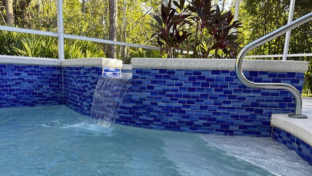 Ein Swimmingpool mit blauen Mosaikfliesen und einem Metallgeländer.