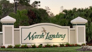 Ein Schild mit der Aufschrift 'Marsh Landing', umgeben von Grünpflanzen und einer Laterne.