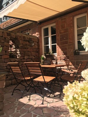 An outdoor patio with stone flooring, a wooden table, and metal chairs. - Vacation apartment "Wildblick" - Stylish living in a historic ambience  (Mürlenbach)