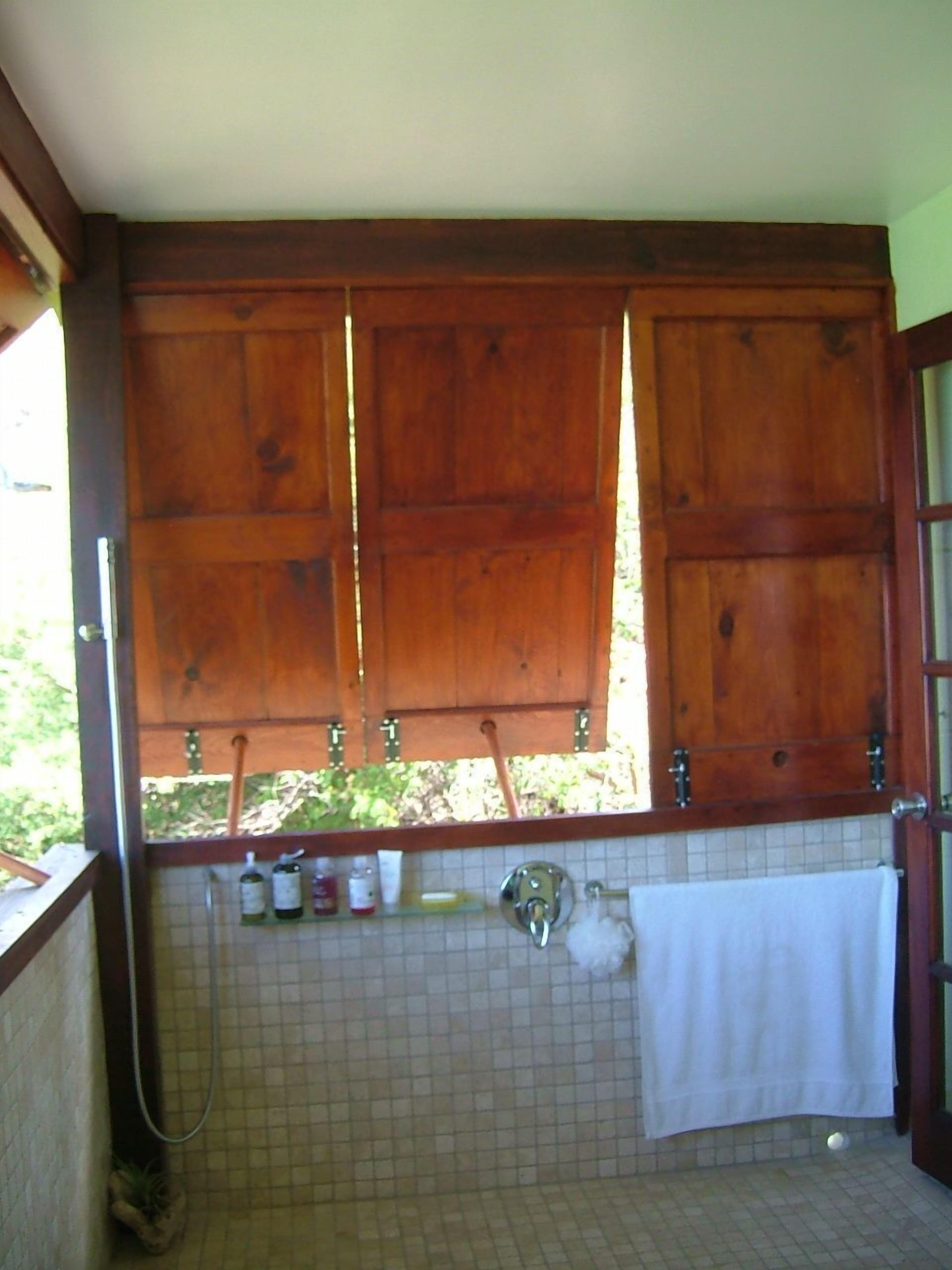 A bathroom with a wooden cabinet above a tiled sink, a towel hanging on the wall, and a shower area with a hose.