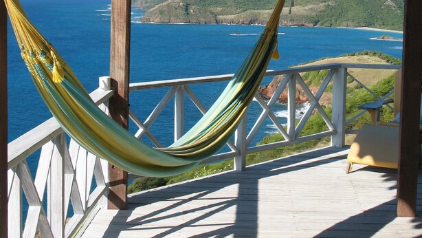 A hammock on a wooden deck overlooking a coastal landscape with hills and the ocean. - Secluded skytop retreat with stunning sea and mountain Views (Falmouth Harbor)