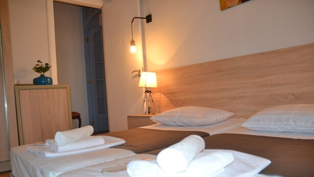 Quarto de hotel com duas camas, uma mesa de cabeceira com abajur e cabeceira de madeira.