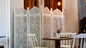 Um quarto com um separador branco detalhadamente esculpido, uma mesa de madeira redonda e duas cadeiras brancas.
