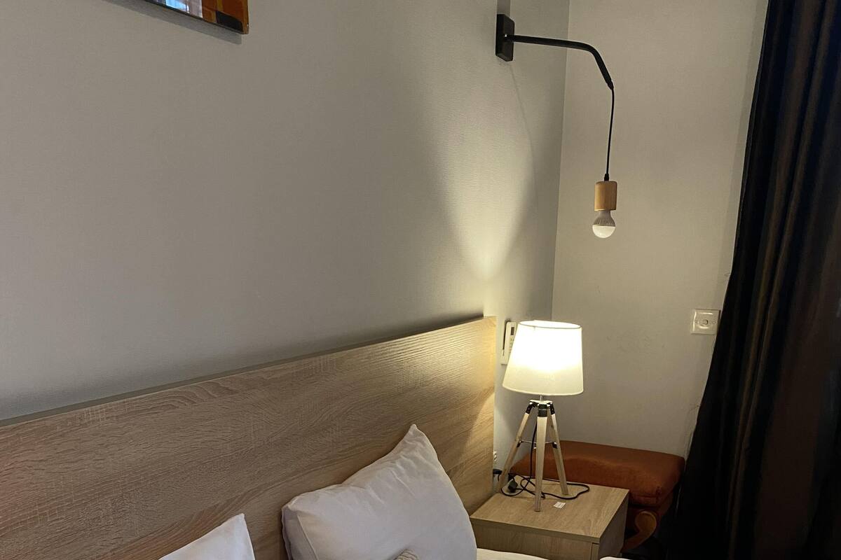 A neatly made bed with white linens and two pillows, a bedside lamp, and a wall-mounted light fixture.