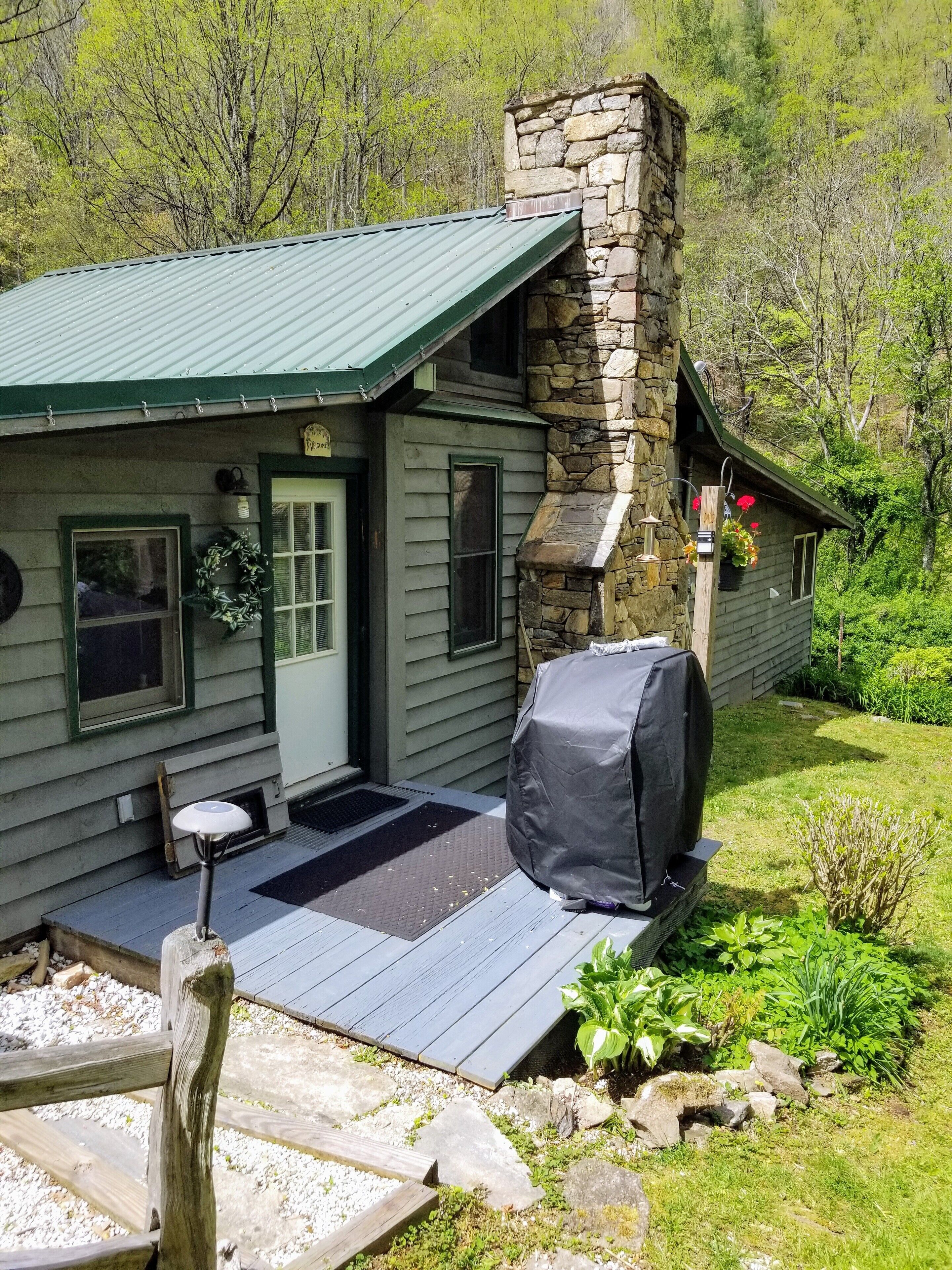 Une cabane rustique avec une cheminée en pierre, un barbecue couvert et une véranda avec un banc.