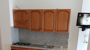 Une cuisine avec des meubles en bois, un plan de travail en granit, une cuisinière et un évier. On y trouve une table à manger avec des chaises et une télécommande posée dessus.