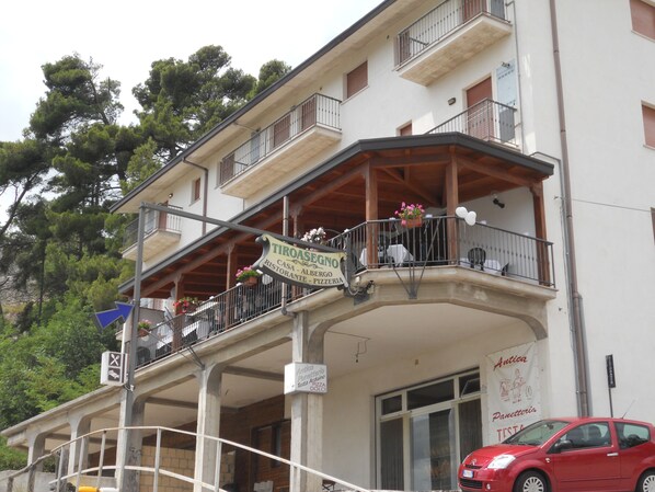 Un immeuble avec un balcon, une enseigne de restaurant et une voiture garée.