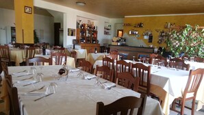 Un restaurant avec de nombreuses tables dressées pour le service, des chaises en bois et un bar avec des étagères remplies de bouteilles.