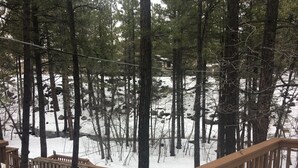Une terrasse en bois, le sol couvert de neige et des arbres en arrière-plan.